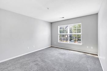 A room with a carpeted floor and a window showing a view of a house.